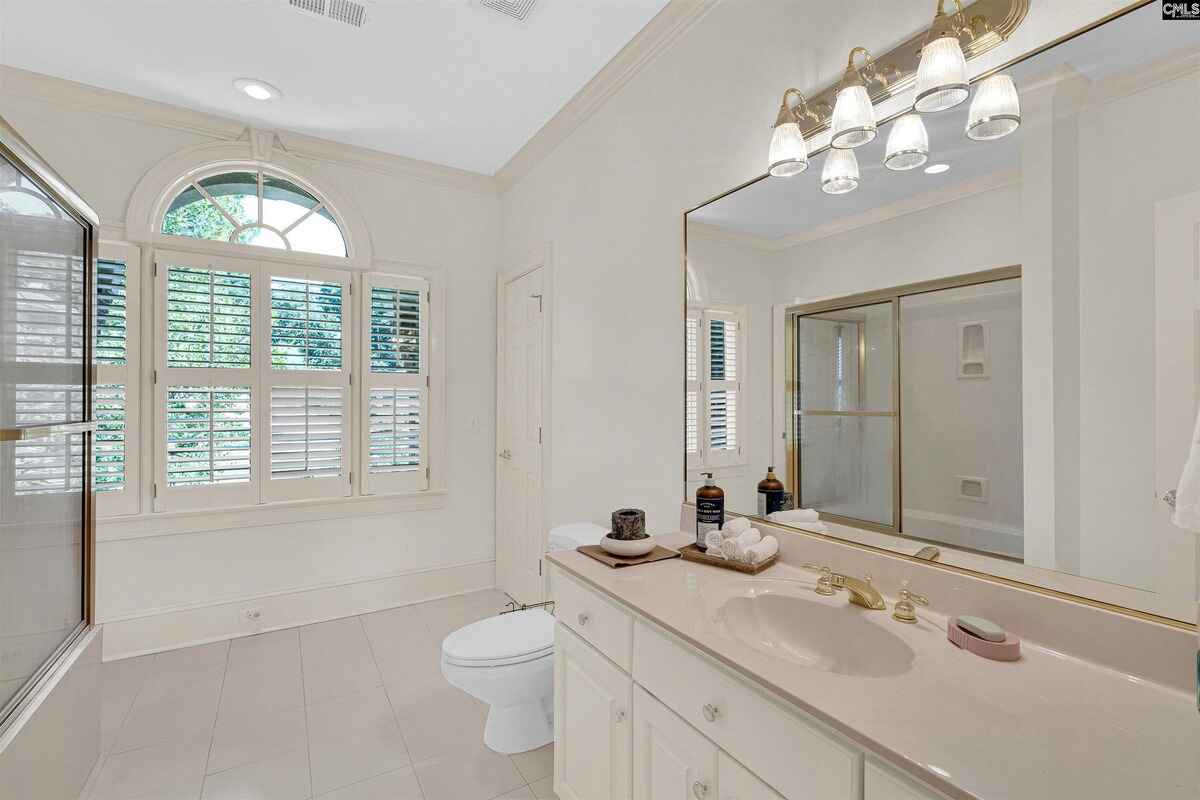 Powder room with a white vanity, shuttered window, and a wall-mounted mirror.