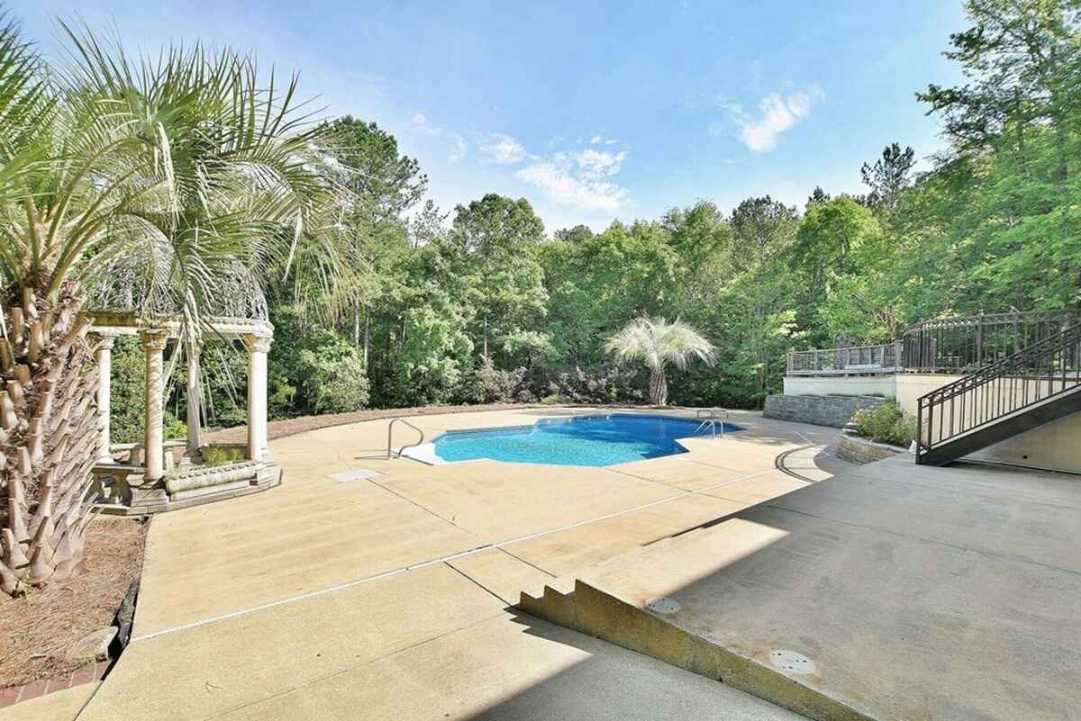 Outdoor pool area is surrounded by lush greenery and includes decorative pillars and a concrete deck.