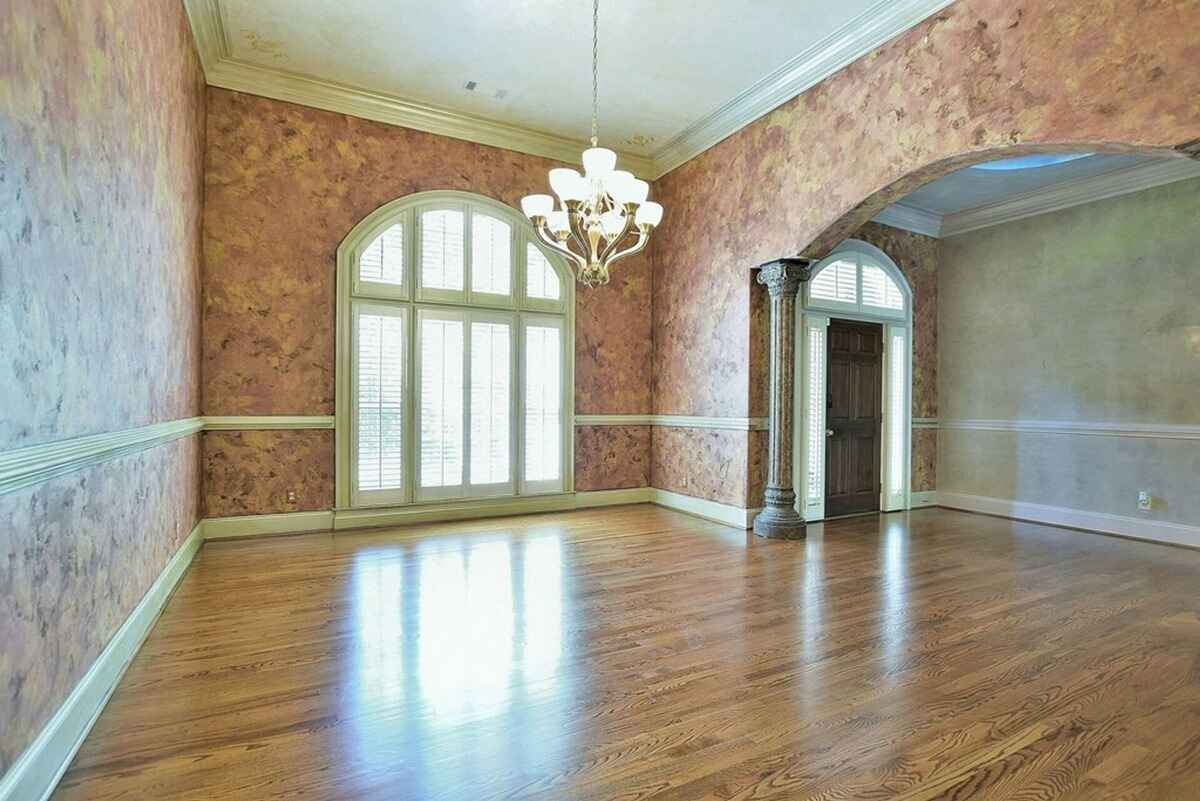 Formal dining room displays large arched windows, hardwood floors, and a detailed ceiling chandelier.