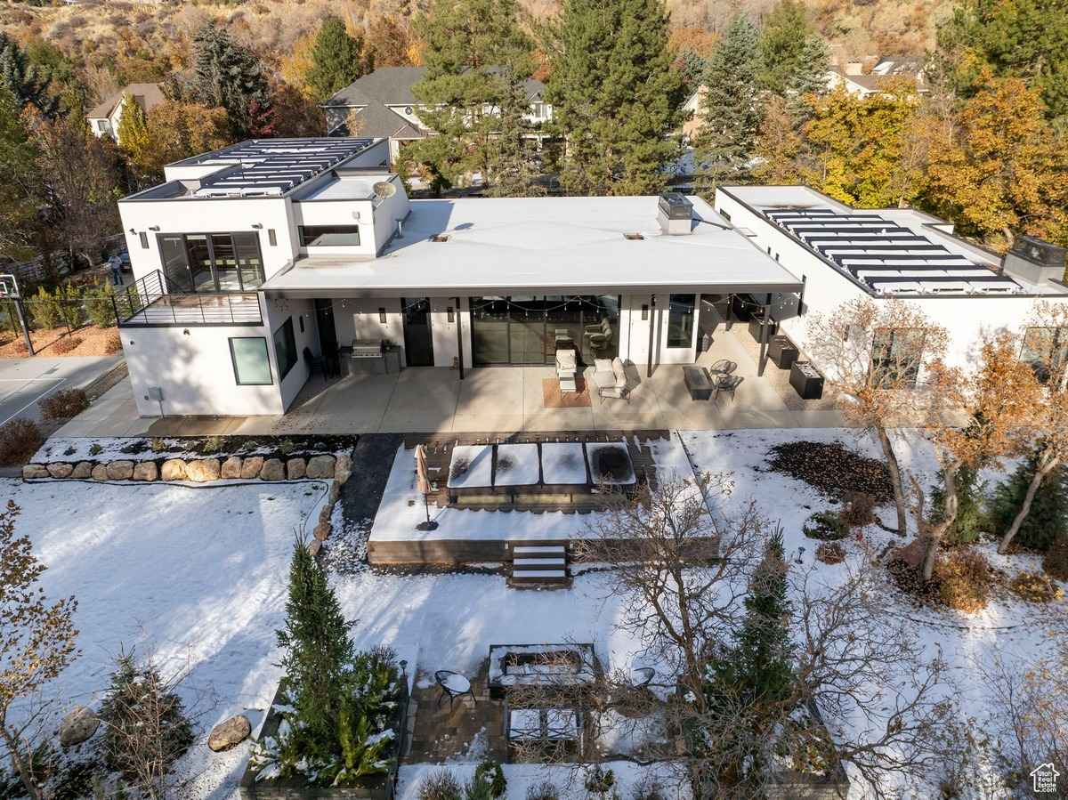 A modern home with a flat roof and large patio area, surrounded by snowy landscaping and trees.