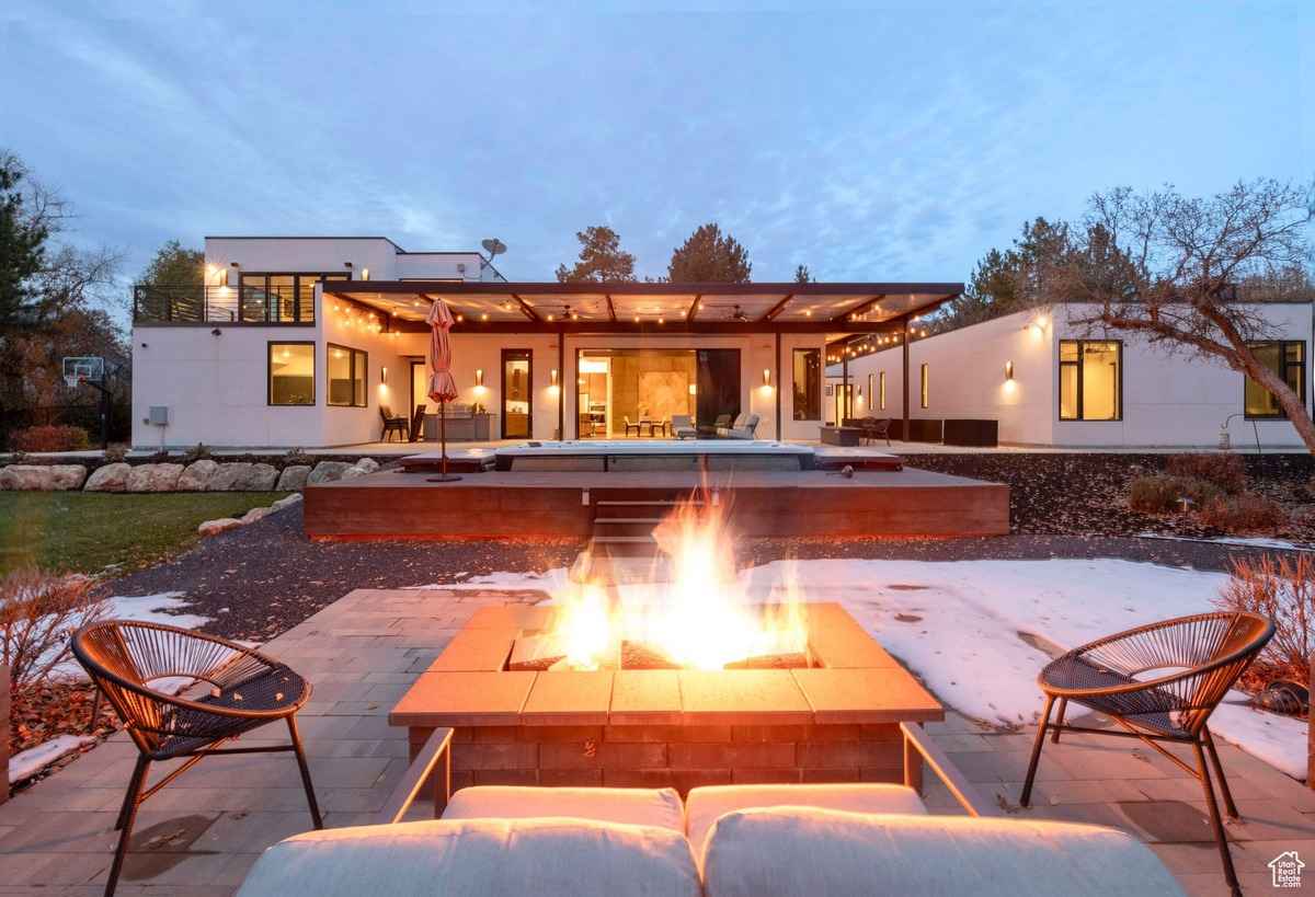 A cozy evening outdoor setup featuring a lit fire pit, modern patio furniture, and warm lighting.