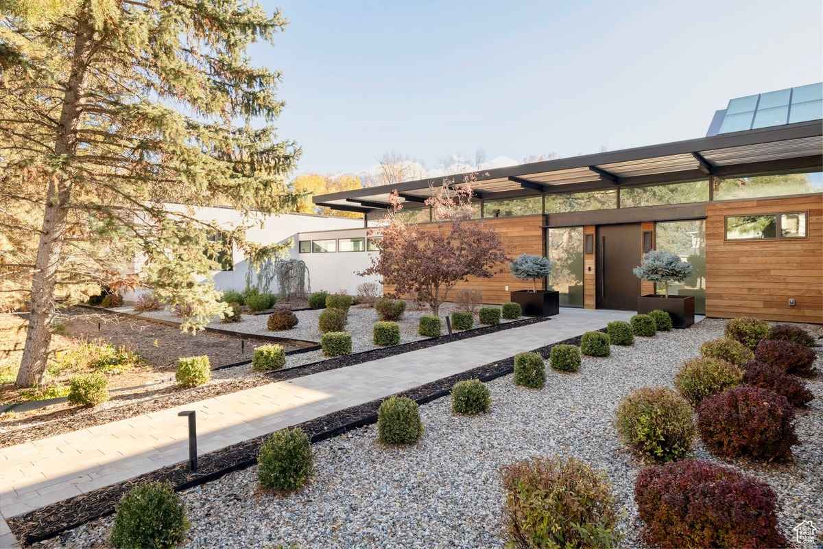 A daytime view of the home's entry with gravel landscaping, neatly trimmed bushes, and a modern design.