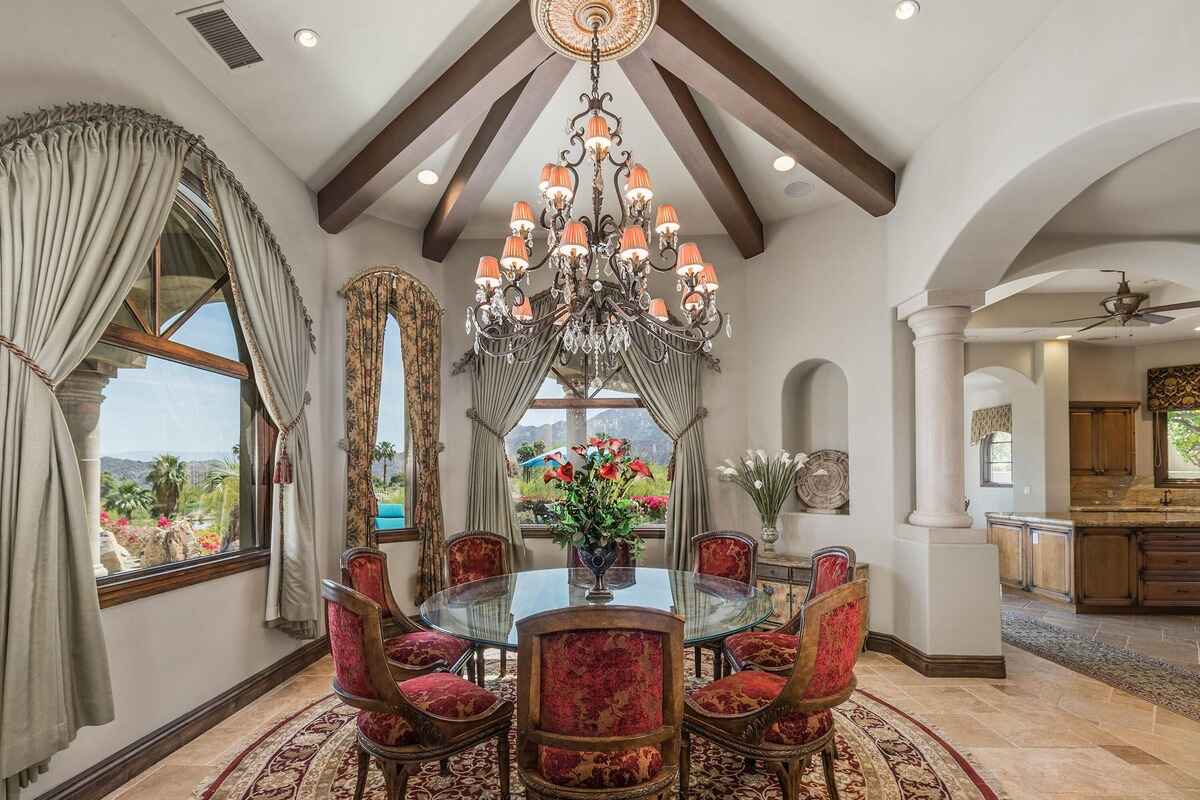 Formal dining room with vaulted ceilings, large windows, and elaborate chandelier above circular table.