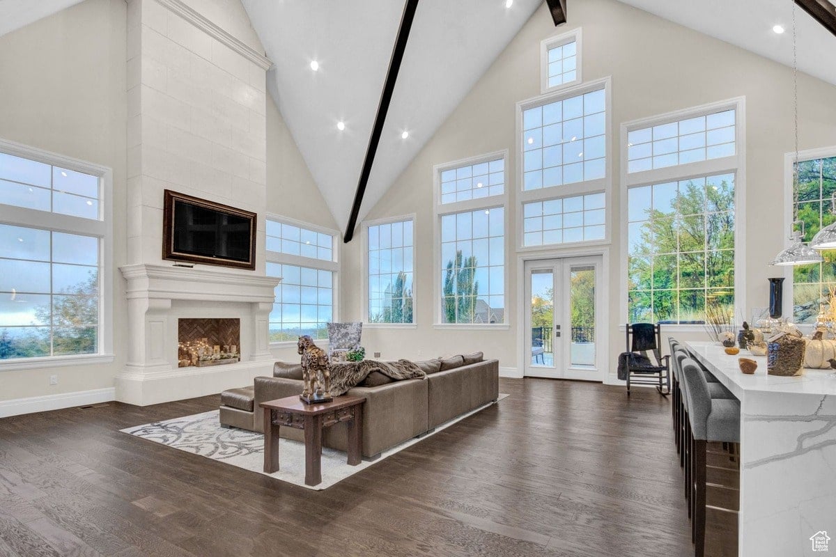 This high-angle shot captures the grandeur of a spacious, open-plan living area, showcasing floor-to-ceiling windows that bathe the room in natural light. The focal point is a large, elegant fireplace with a mounted television above, creating a warm and inviting atmosphere.