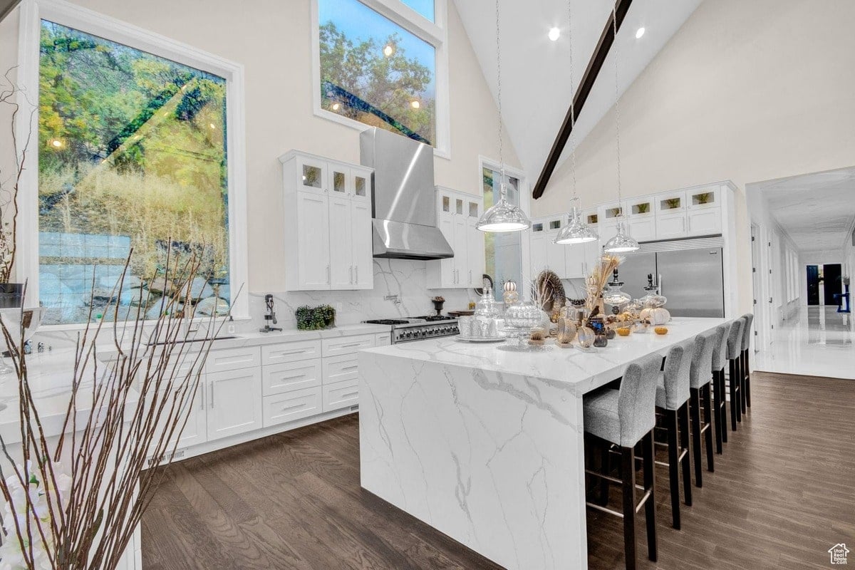 This kitchen's design is a masterpiece of modern elegance, featuring a large island with seating, custom cabinetry, and a high-end range hood. The high ceilings and expansive windows create a sense of openness and grandeur.