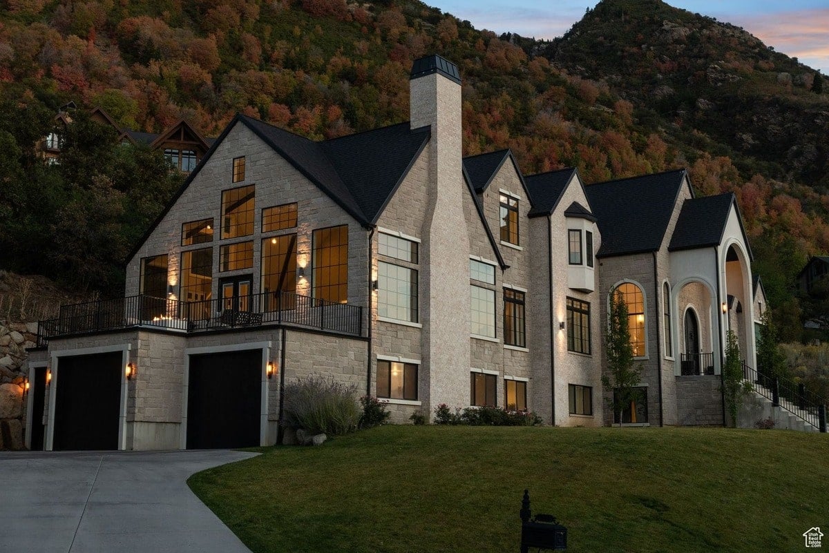 A sophisticated interplay of textures and light defines this remarkable residence, where the warmth of natural stone is balanced by the sleek lines of the dark roof and window frames. Nestled on a hillside, it commands breathtaking views of the surrounding landscape.