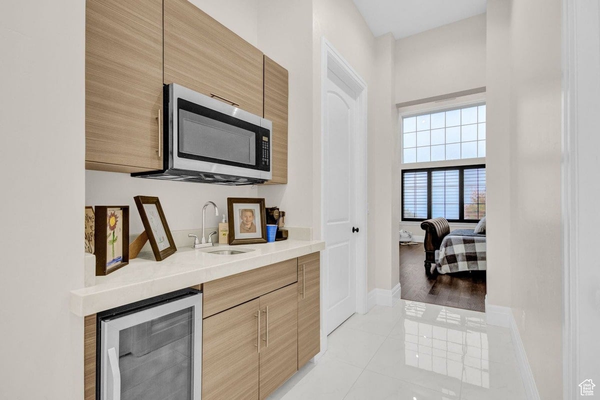 This view captures a stylish and functional wet bar tucked away in a hallway, providing a convenient space for drinks and snacks. The light-colored cabinetry and minimalist design complement the overall modern feel of the home, offering a peek into an adjacent bedroom.