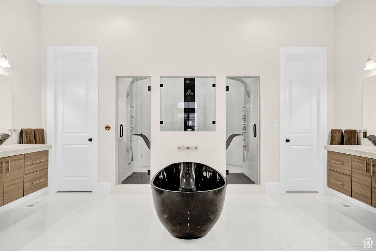 A contemporary bathroom is presented in this photograph, highlighting its clean lines and symmetrical layout. The dark, sculptural bathtub is the centerpiece, framed by two glass-enclosed showers and light wood vanities, creating a sense of modern sophistication.