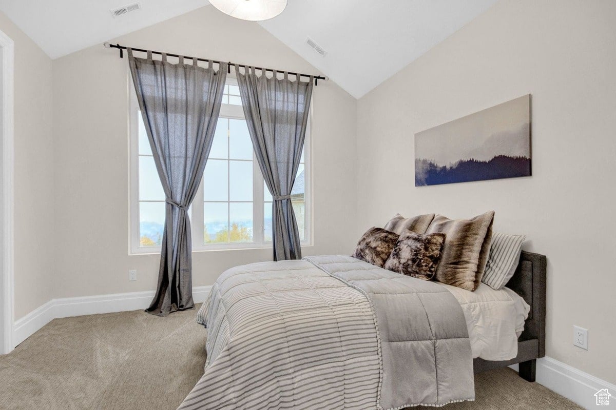 This tranquil bedroom features a comfortable bed dressed in a striped comforter, complemented by a large window with gray curtains. A calming landscape painting above the bed adds a touch of serenity to the space.