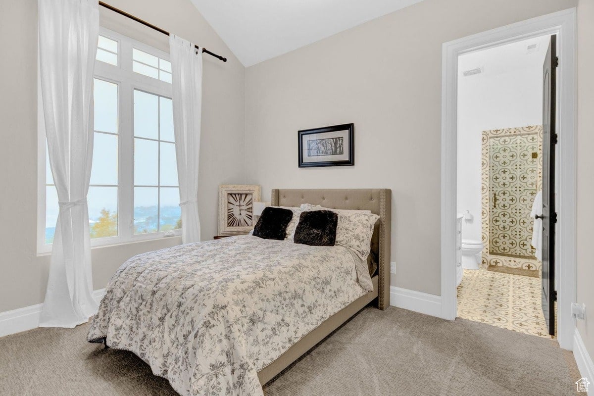 This bedroom's calming design features a floral comforter on a neutral-toned bed, set against a light gray wall. A glimpse into an en-suite bathroom with patterned tile flooring adds a touch of visual interest.