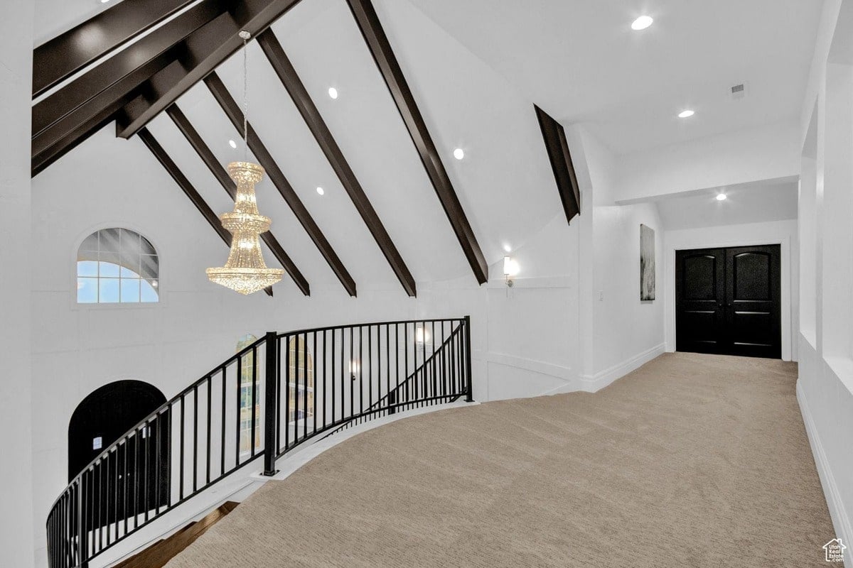 This dramatic architectural detail showcases a curved upper hallway with a black metal railing overlooking a grand staircase. A stunning crystal chandelier hangs below, adding elegance to the high-ceilinged space.