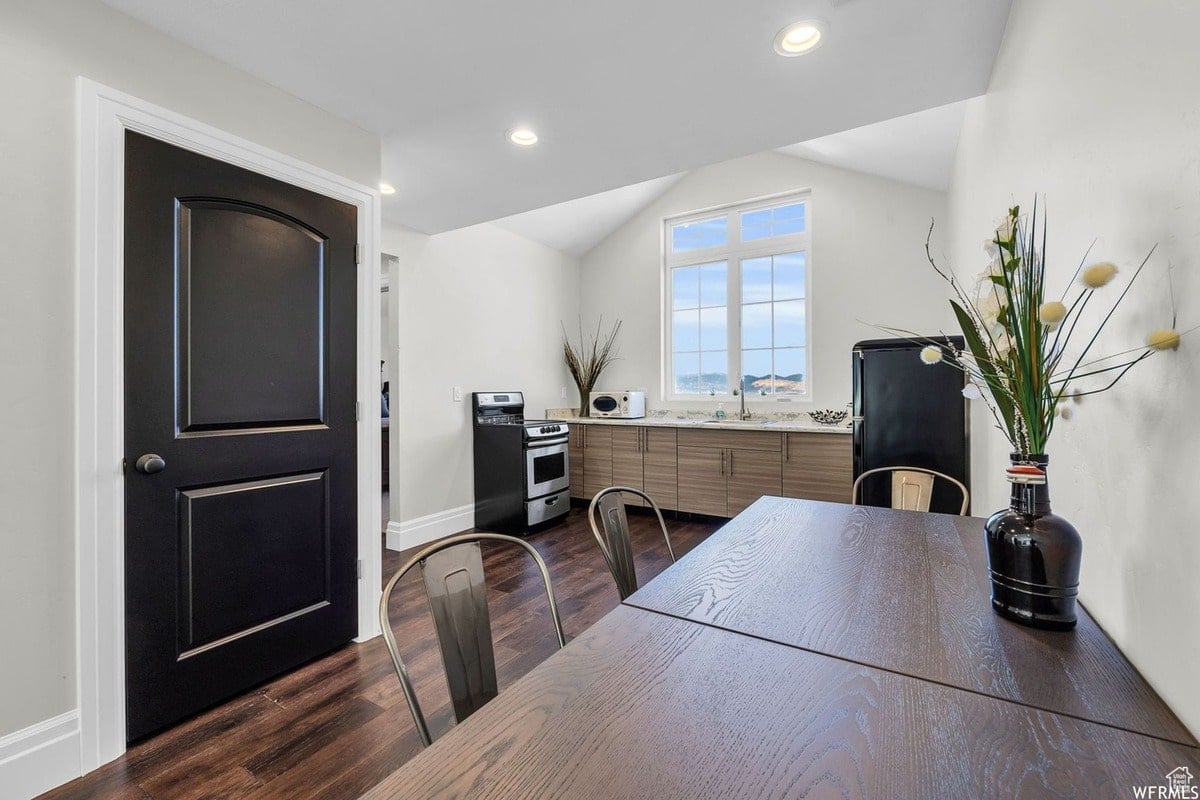 This bright kitchen features a farmhouse-style design with light wood cabinets and a large window offering a scenic view. A dark wood dining table with metal chairs sits conveniently near the kitchen, creating a comfortable and functional space.