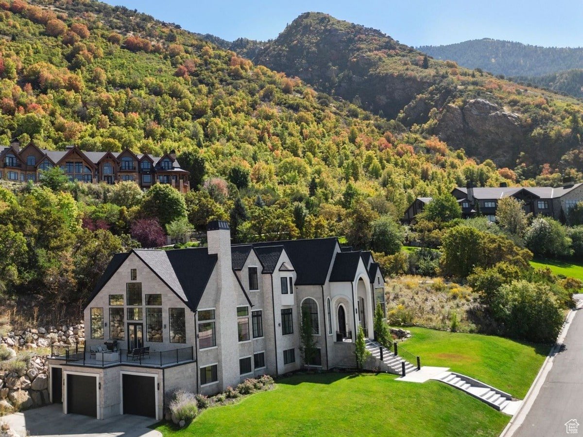 An aerial perspective showcases this stunning residence nestled amongst the fall foliage of a mountainside. The home's unique design, complete with a spacious attached garage and elevated deck, complements its picturesque location.