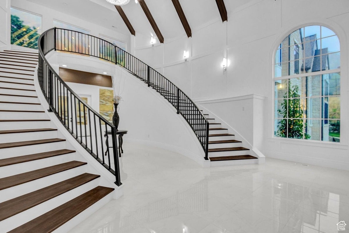This wide-angle shot reveals a luxurious home's grand entrance, featuring a curved staircase that draws the eye upward. The clean lines and minimalist aesthetic create a sense of elegance and spaciousness, enhanced by the natural light from the large window.