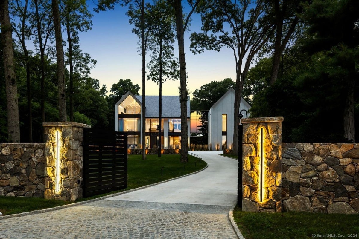 Mansion entance and driveway curves gently towards a large, contemporary house, and the entrance is marked by stone pillars with integrated lighting.