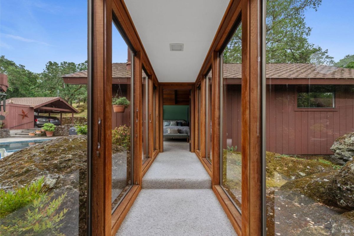 Glass-enclosed hallway connects separate sections of the house, offering views of the natural surroundings.