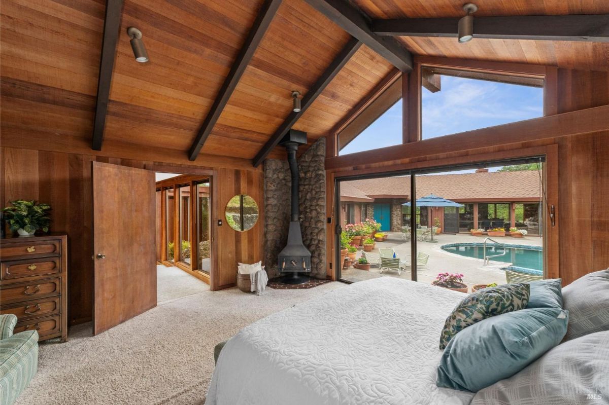 Warm-toned room highlights a wood-burning stove, vaulted ceilings, and a pool view from sliding doors.