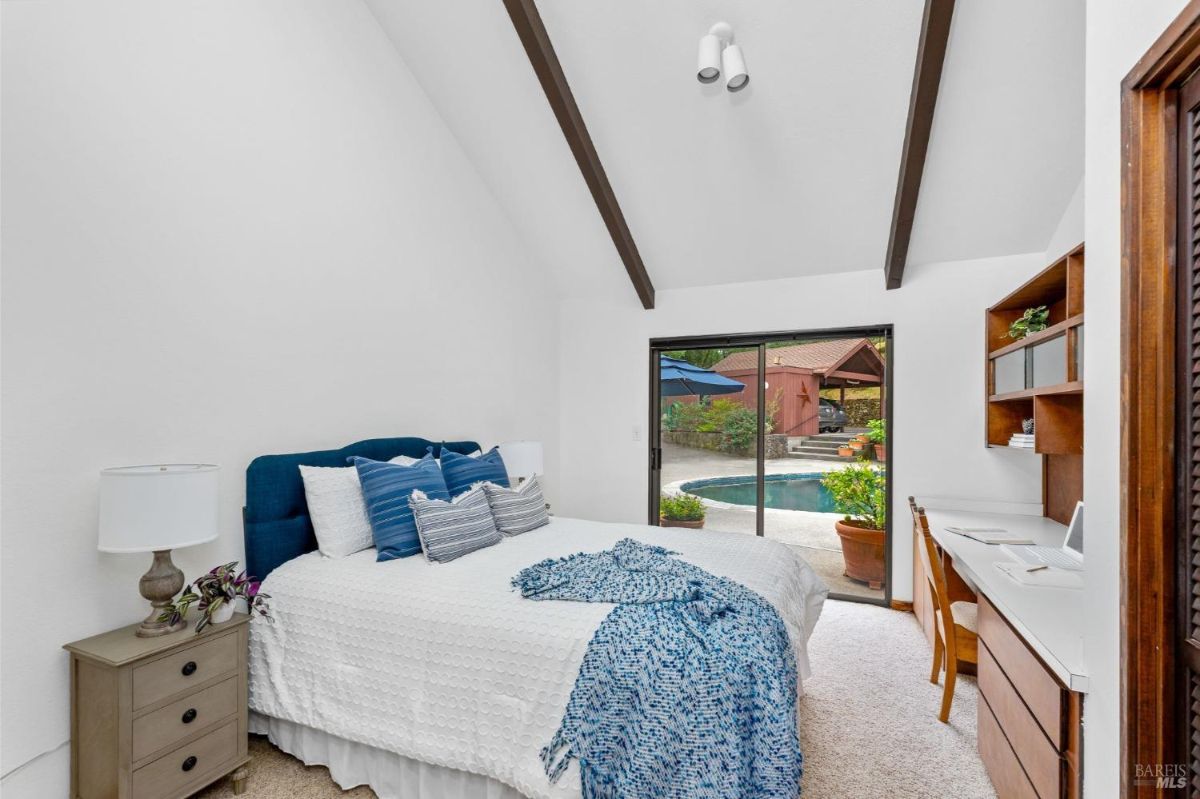 Spacious bedroom includes a vaulted ceiling, blue-accented bed, and access to the pool area.