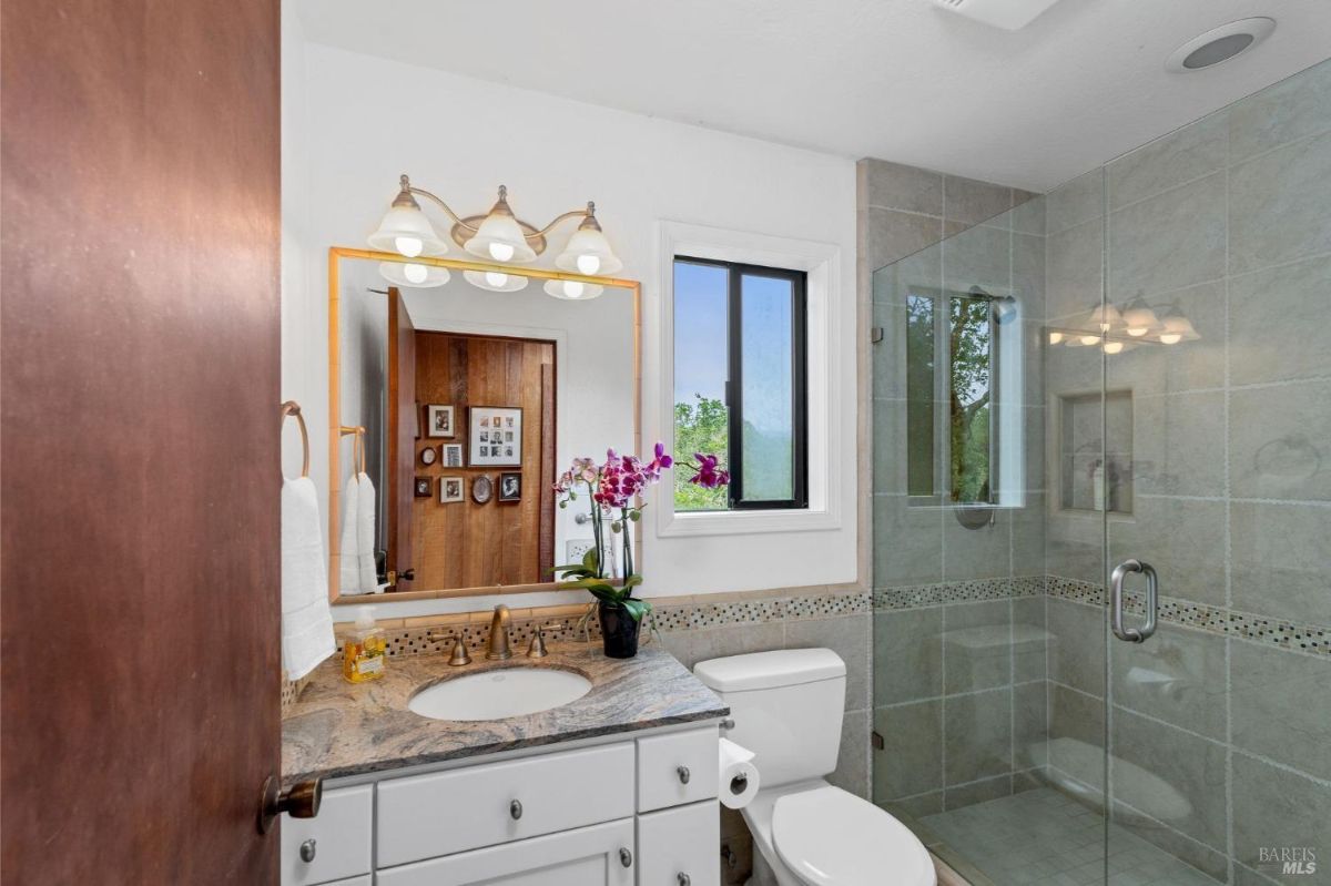 Compact bathroom showcases a granite countertop, a shower, and a window with natural light.