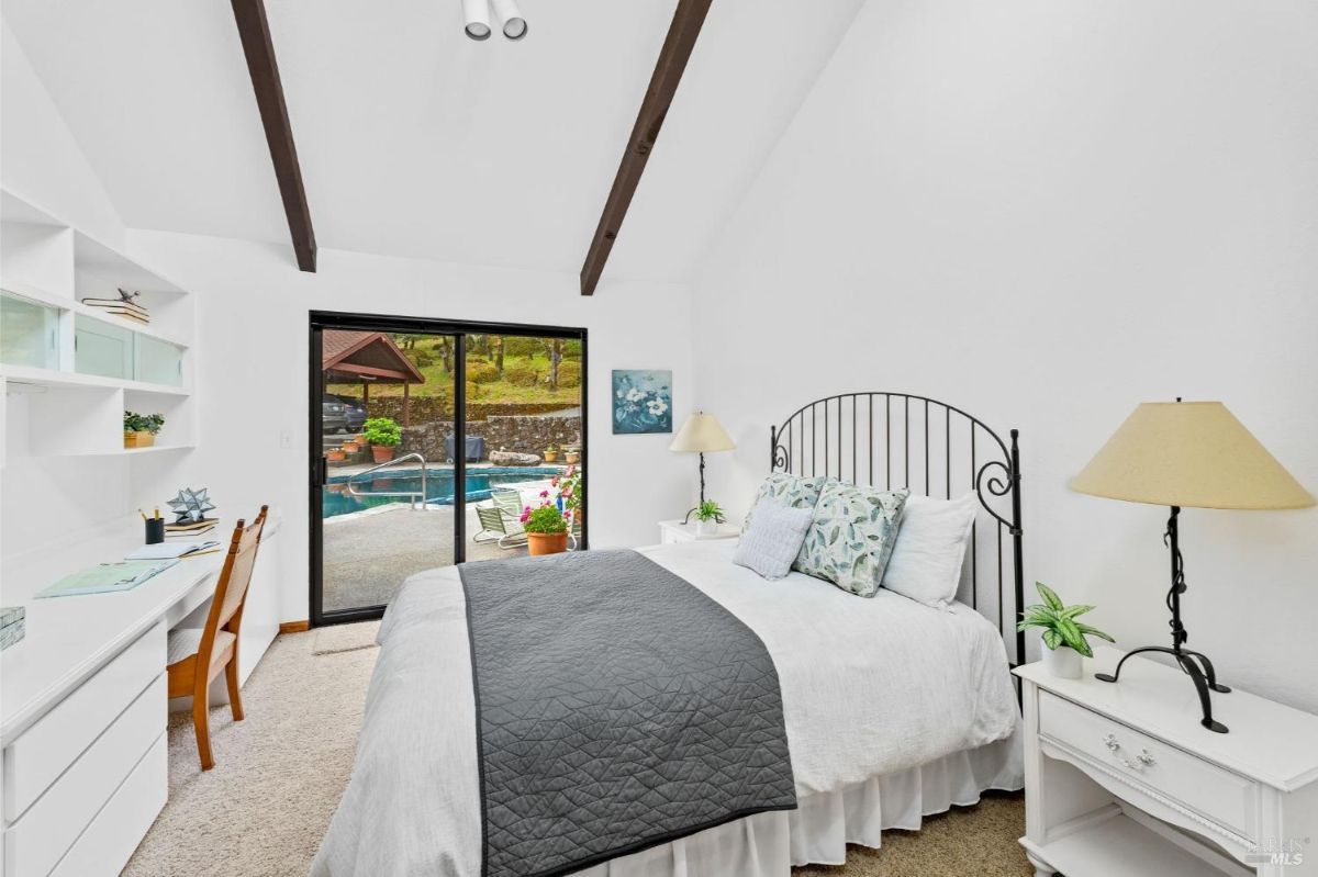 Bright bedroom with white walls, a small desk, and a poolside view through glass doors.
