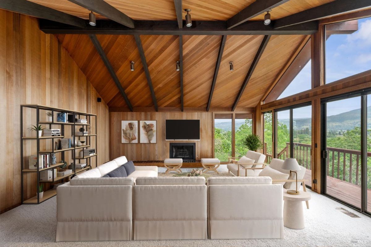 Cozy sitting room featuring warm wood-paneled walls, a central fireplace, and a serene view of the greenery outside.