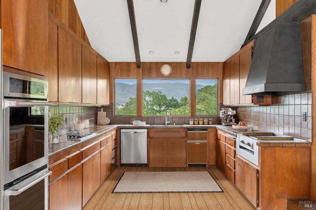 Kitchen with a U-shaped layout, tiled backsplash, and expansive windows overlooking greenery.