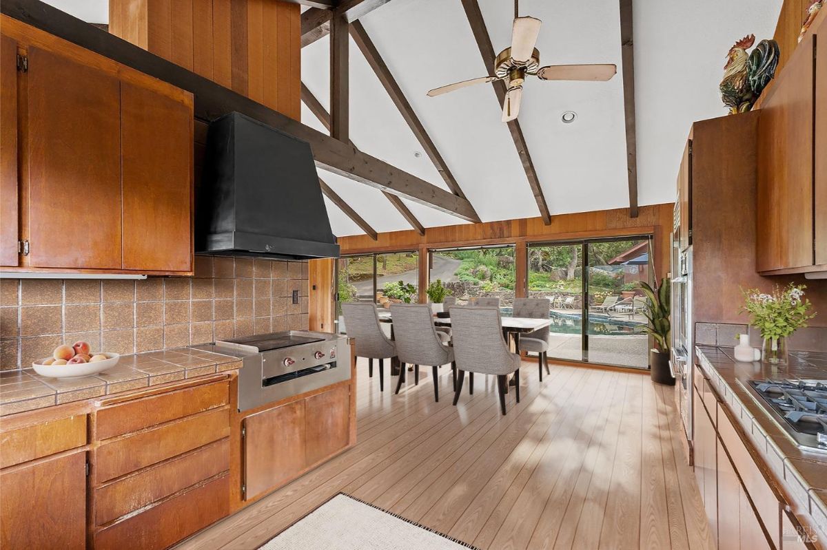 Kitchen and dining area with exposed beams, a black range hood, and large windows showcasing outdoor views.