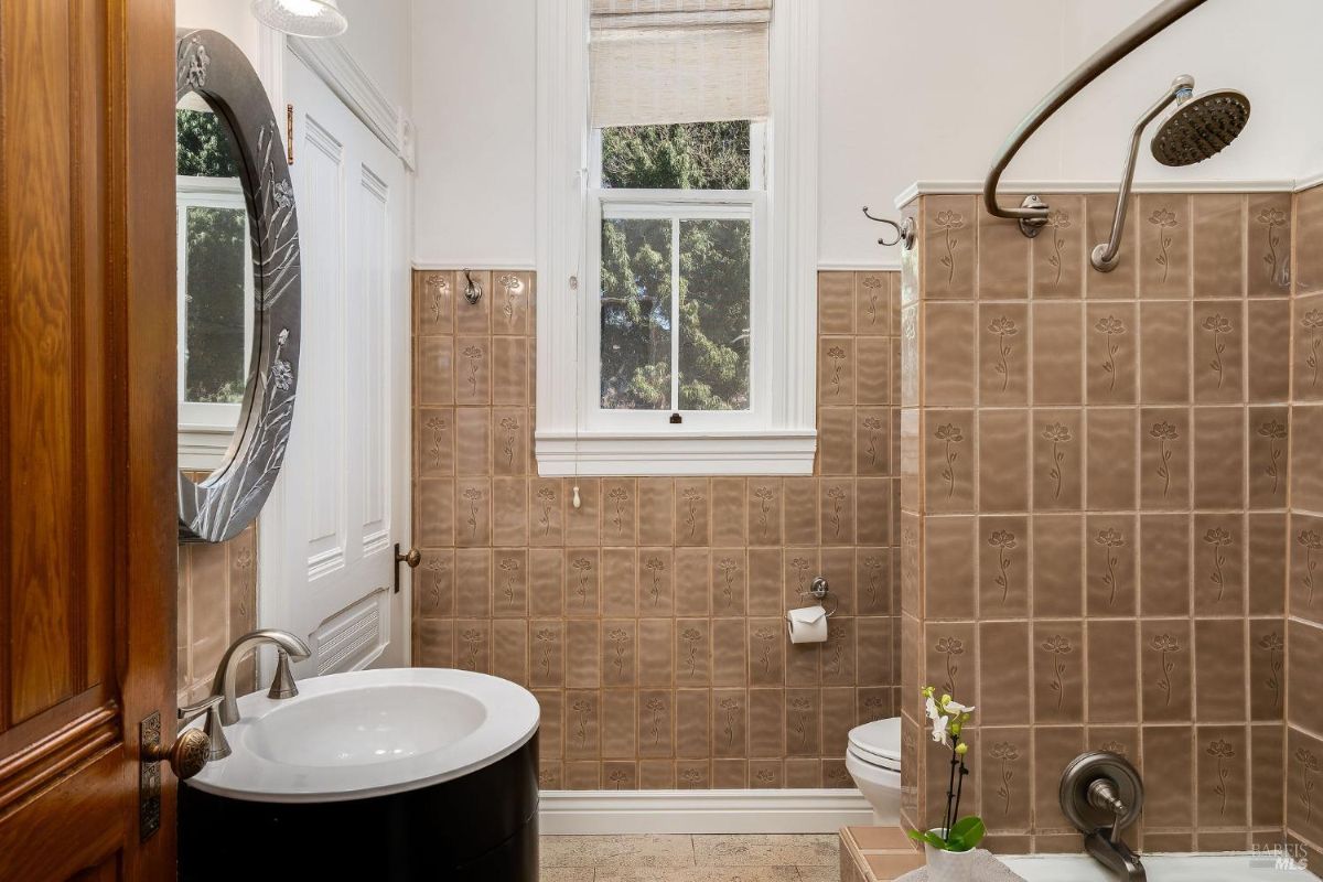 Compact bathroom with beige tiled walls, a round mirror, and a curved shower rod.