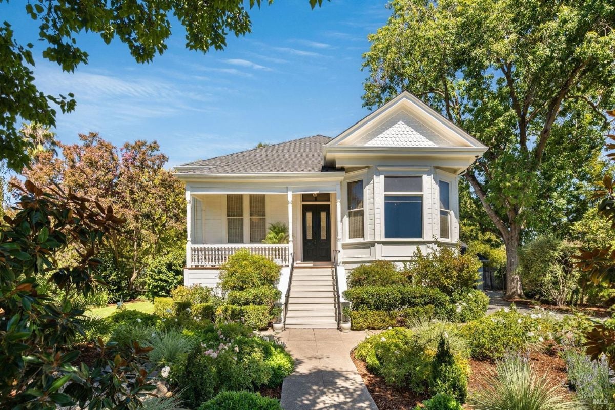 Exterior of a classic house with a front porch, lush garden, and a staircase leading to the entrance.