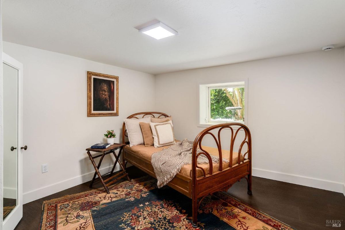 Small bedroom with a metal-frame bed, wooden furniture, and a floral rug on a dark floor.
