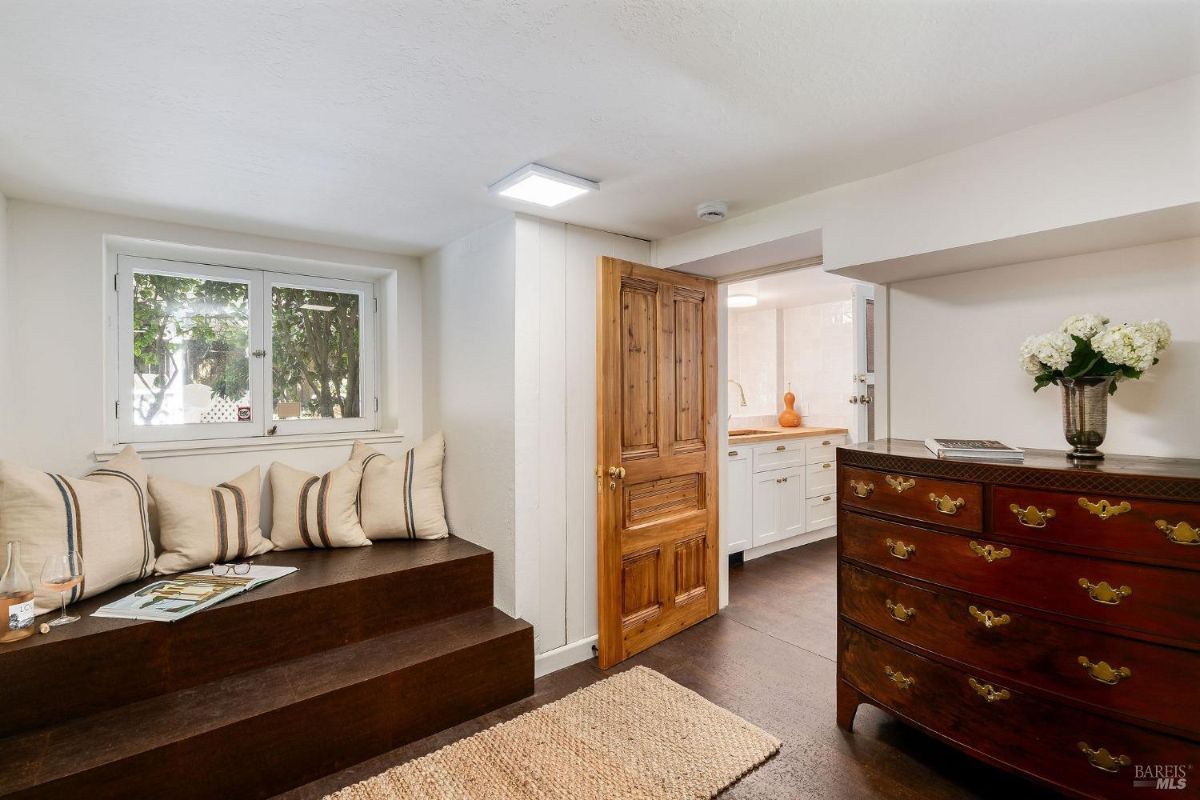 Room with a small window seat, dresser, and wooden door leading to a kitchenette.