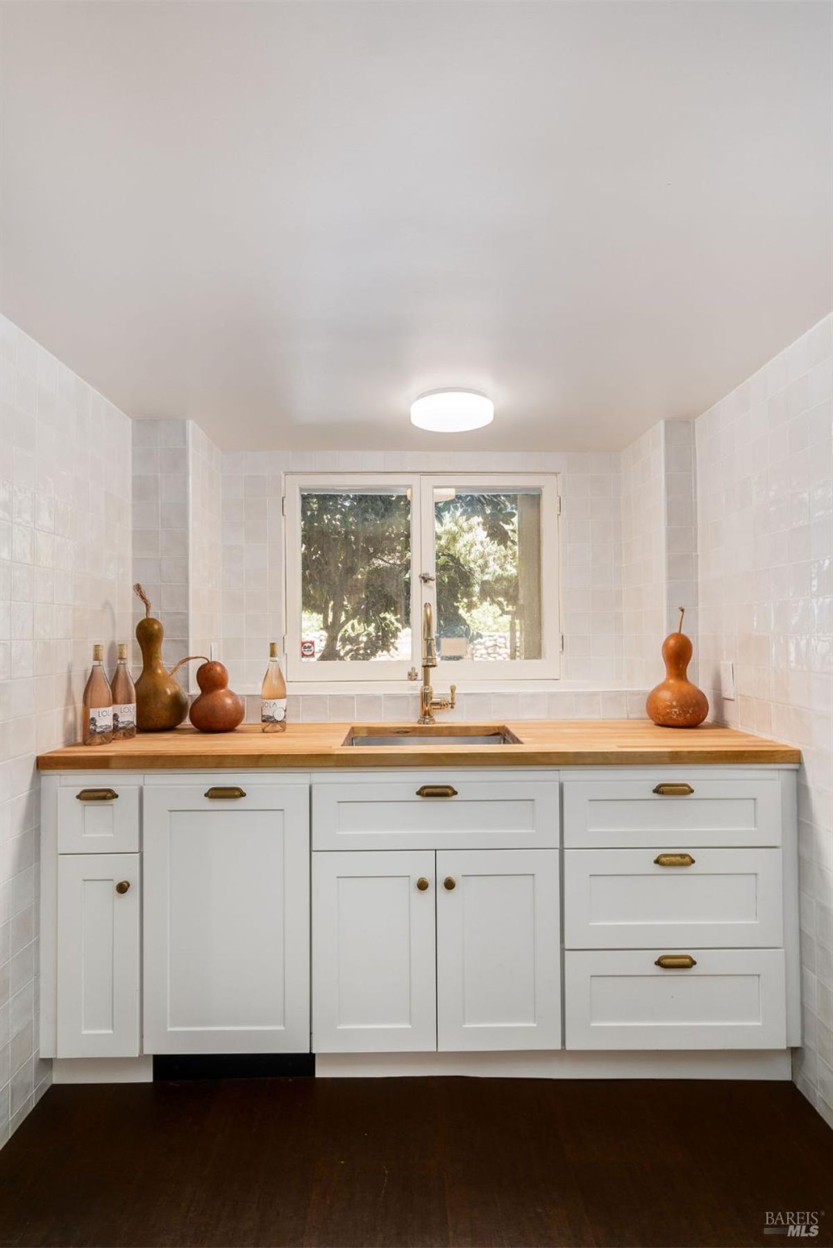 Compact kitchen space with white cabinets, wood countertops, and a central window view.