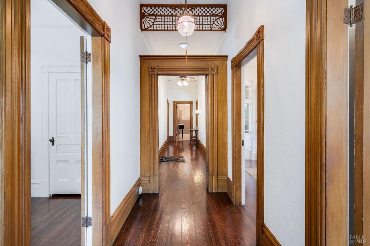 Hallway with wooden doorframes and polished hardwood floors, leading to multiple rooms.
