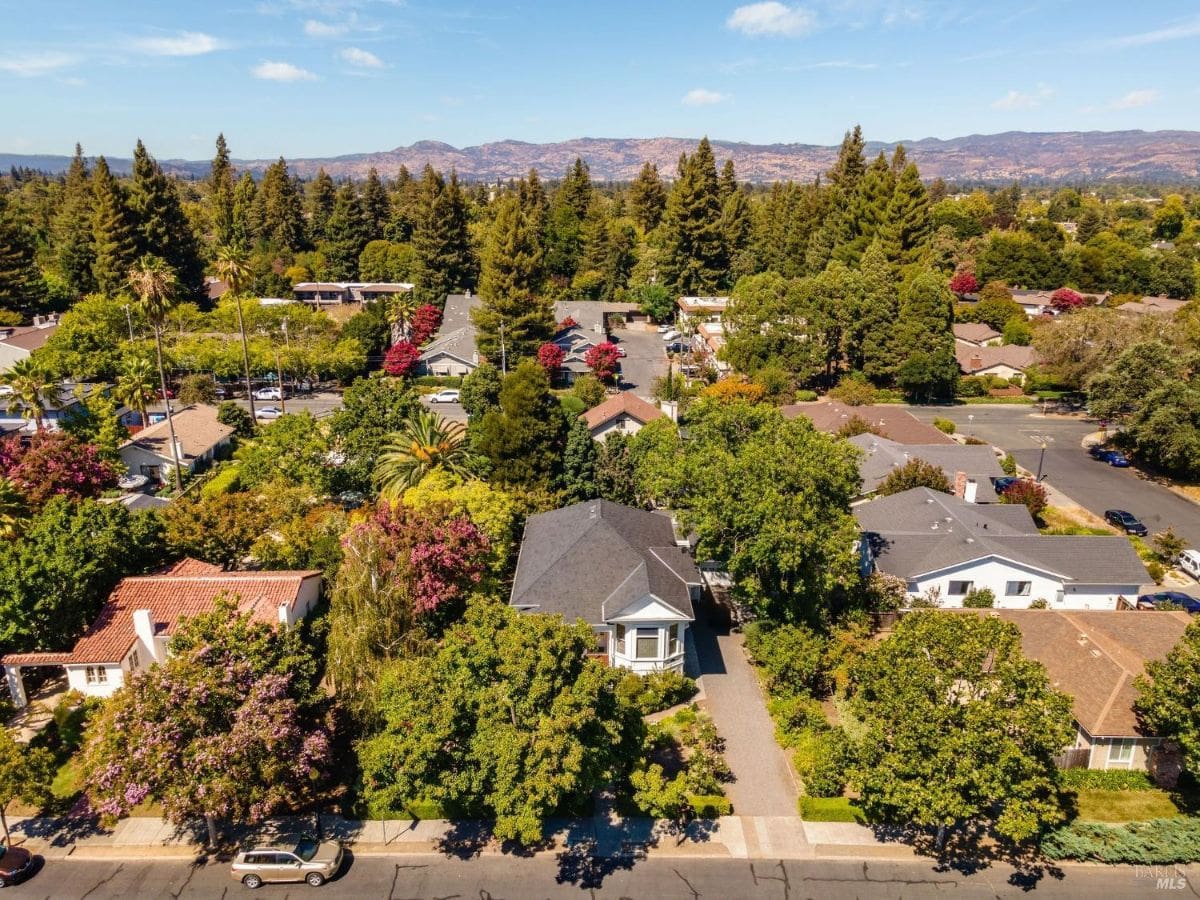 Aerial view of a neighborhood with trees, houses, and mountains in the background.