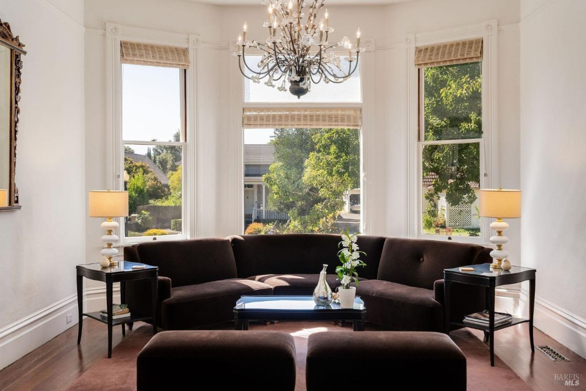 Living room featuring a curved dark brown sofa, tall windows, and a chandelier.