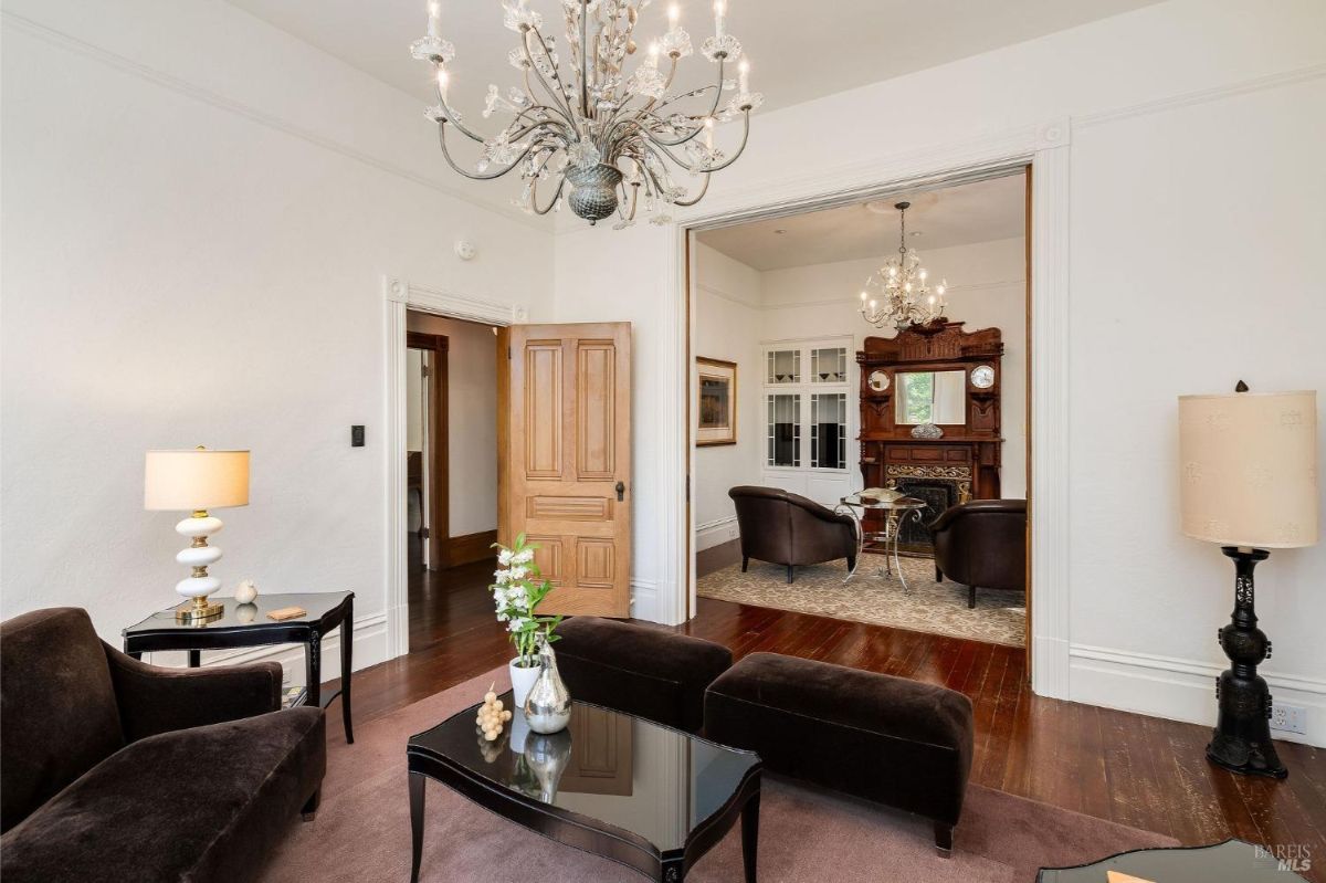 Open doorway connecting two living areas with classic furnishings and a wooden fireplace.