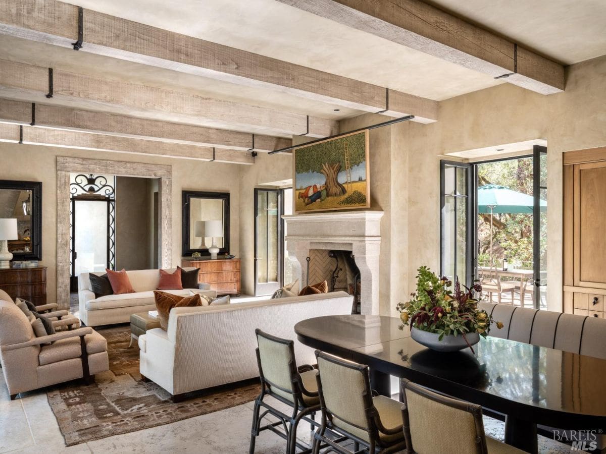 Another view of a rustic living room, highlighting a dining table and additional seating arrangements near the fireplace. The room features earthy tones and a harmonious blend of vintage and contemporary styles.