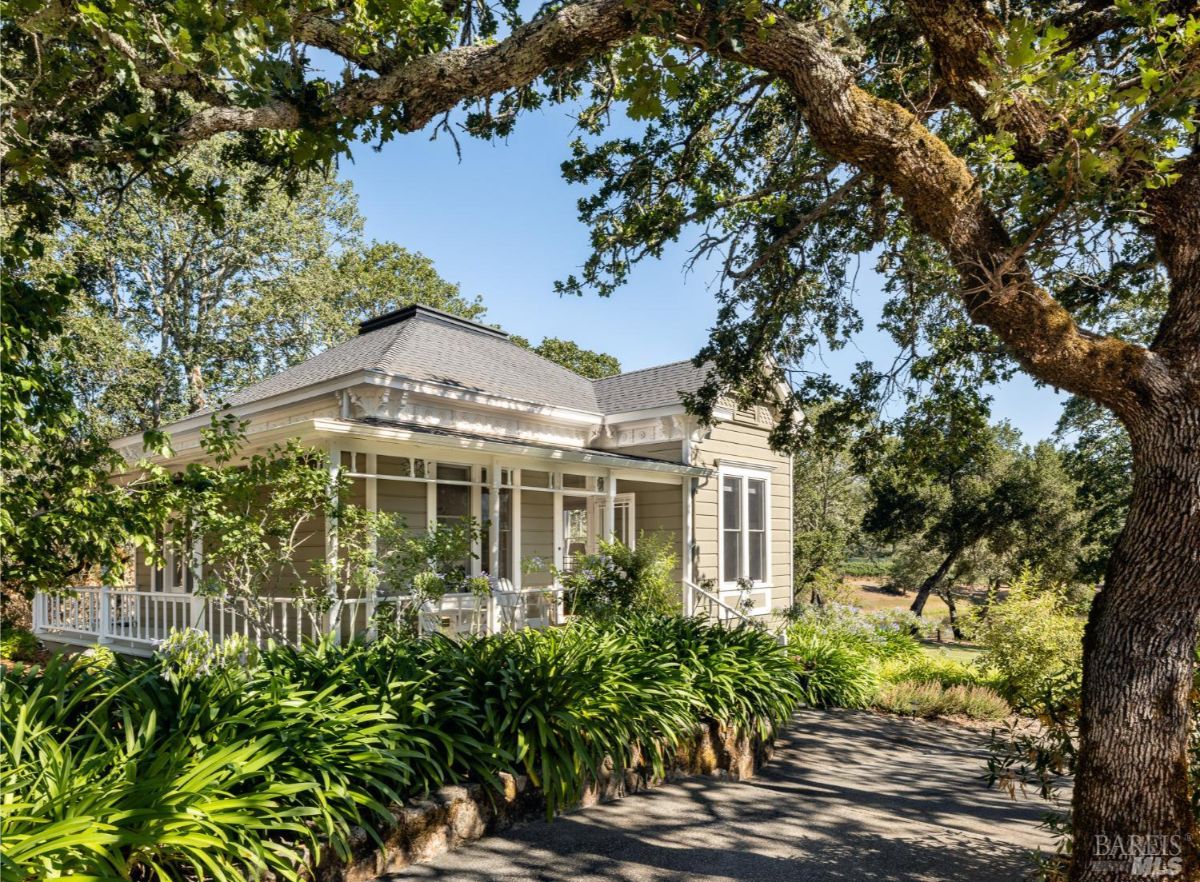A side view of the green house reveals its intricate architectural details, including a wraparound porch and lush landscaping, emphasizing its classic beauty.
