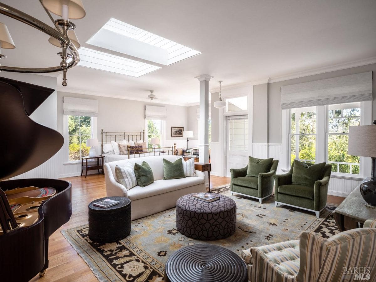 A bright and elegant living space with a skylight, a grand piano, cozy seating, and tasteful decor. The room combines classic and modern design elements with ample natural light.