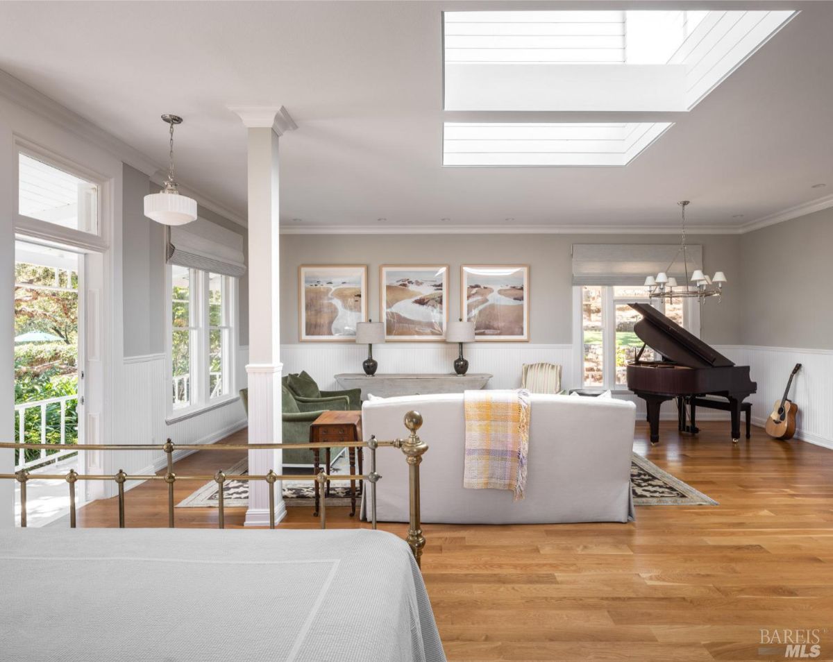 A living space with a combination of a bedroom and lounge, featuring a skylight, a bed, a piano, and a sitting area. The room is designed with light tones and offers an airy, open feel.