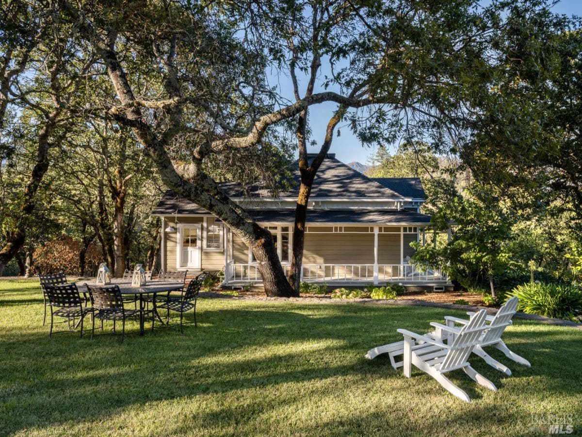 The rear of the house features a lawn with outdoor seating and dining arrangements under a canopy of trees. This space is ideal for relaxing and entertaining outdoors.