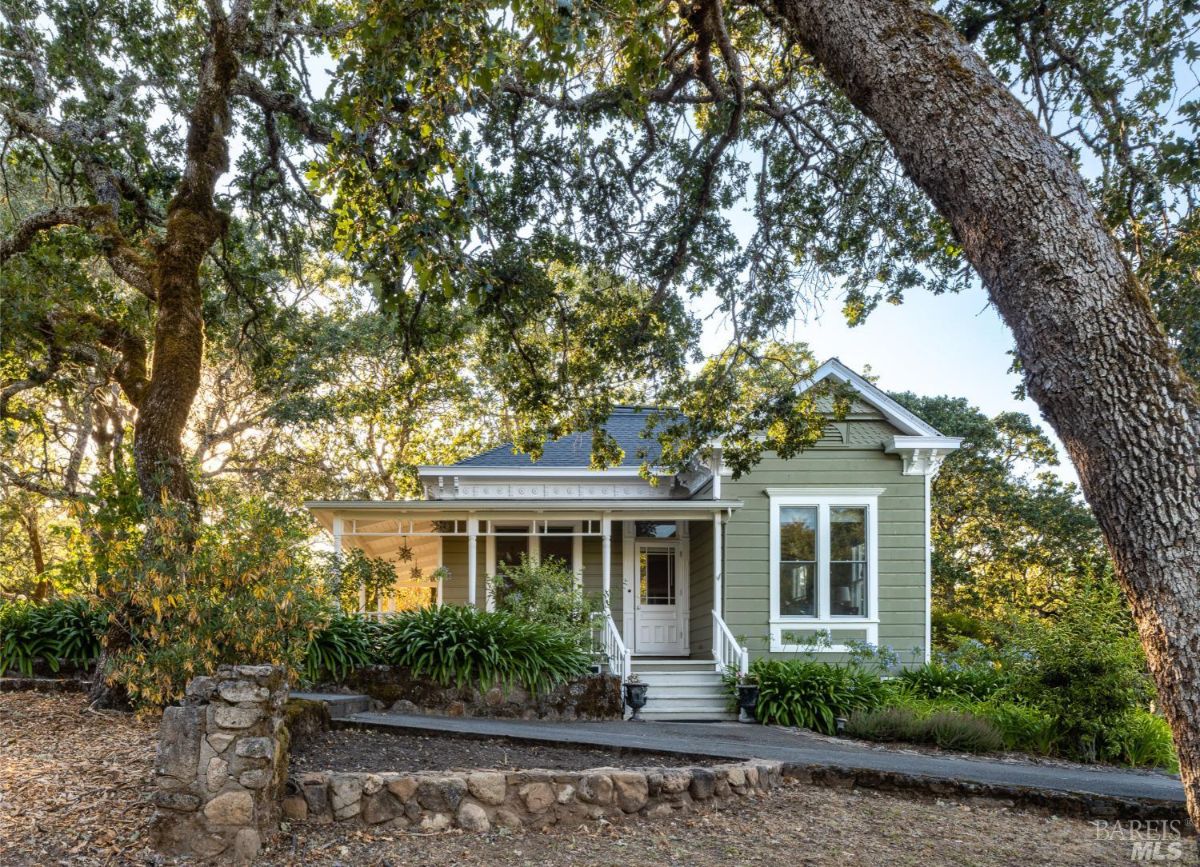 A traditional green house with white trims and a front porch, surrounded by vibrant greenery. The setting exudes timeless charm and coziness.