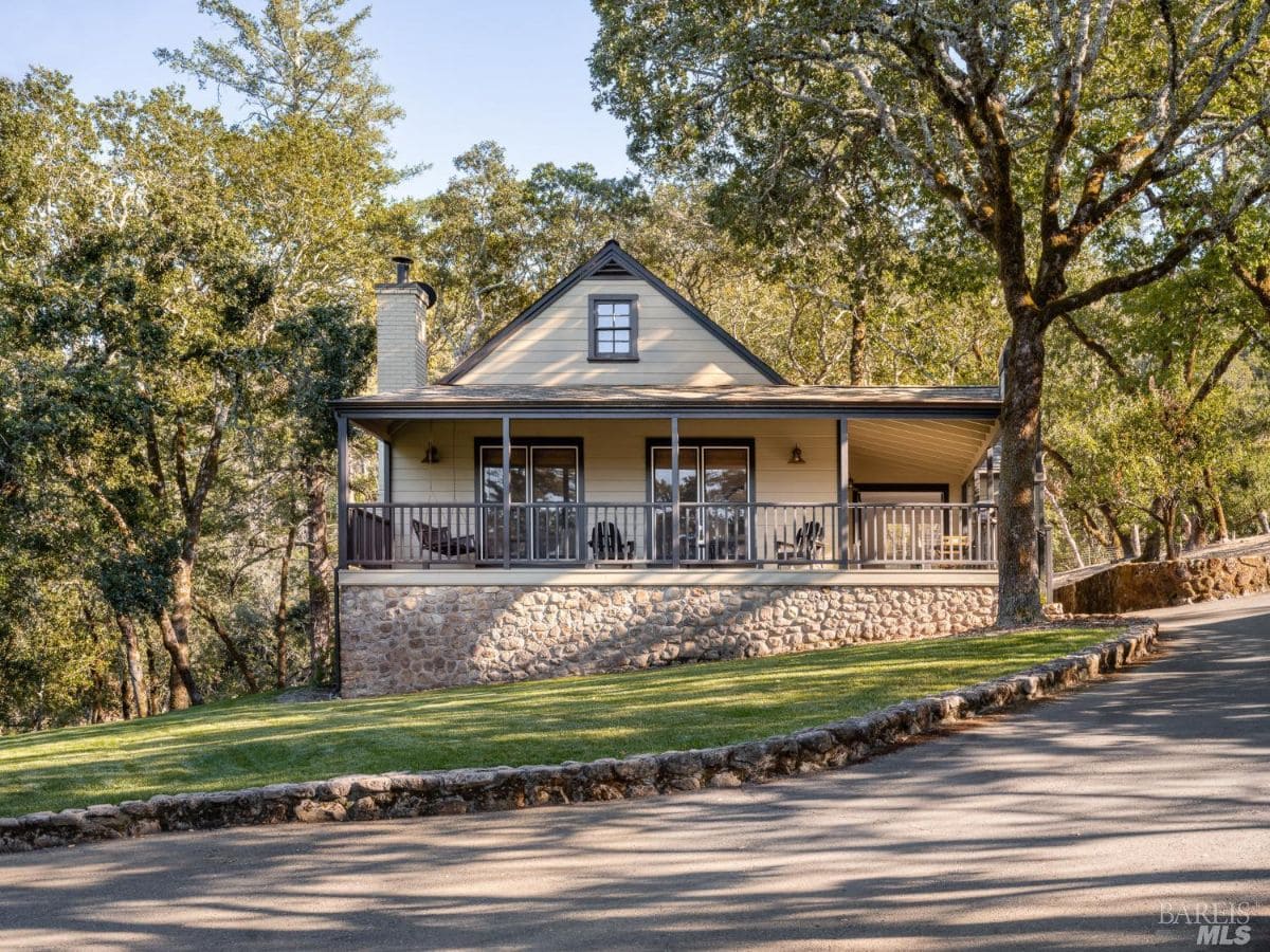 A cottage-style home with a stone foundation, a cozy porch, and a slanted roof. The well-maintained driveway and lawn enhance the property's inviting appeal.