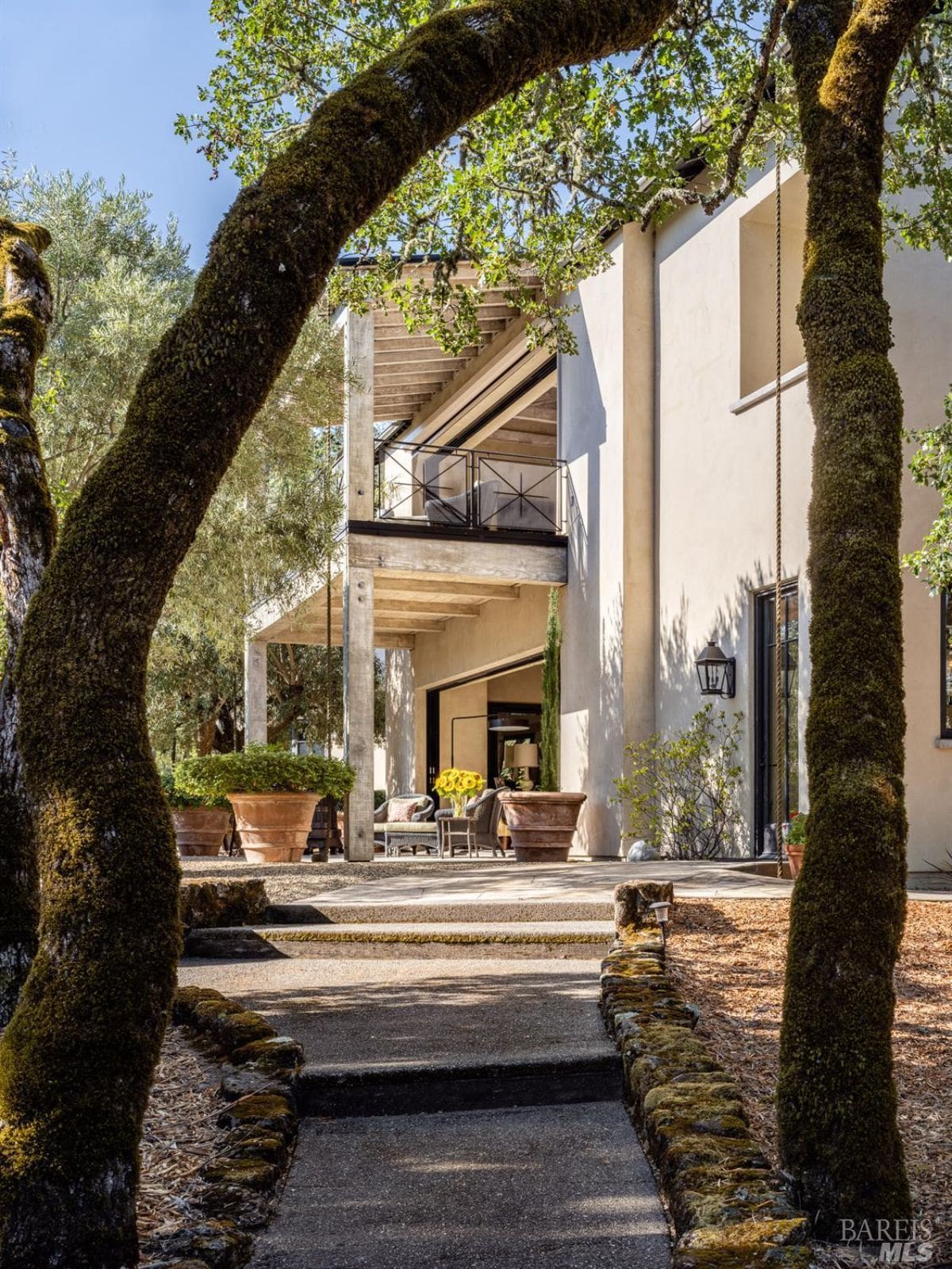 A close-up of the home’s architectural details with a walkway framed by moss-covered trees leading to an outdoor seating area.