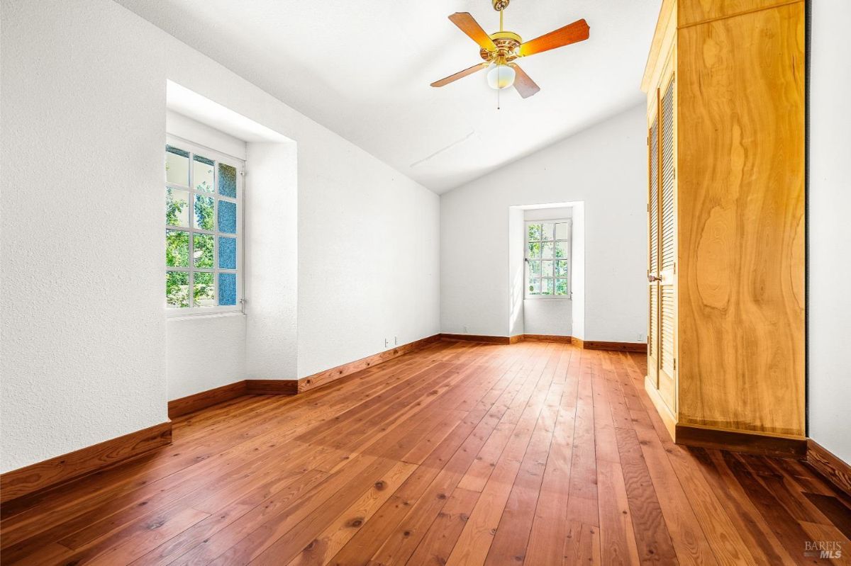 A room with wood floors, white walls, a ceiling fan, and windows at both ends for cross ventilation.