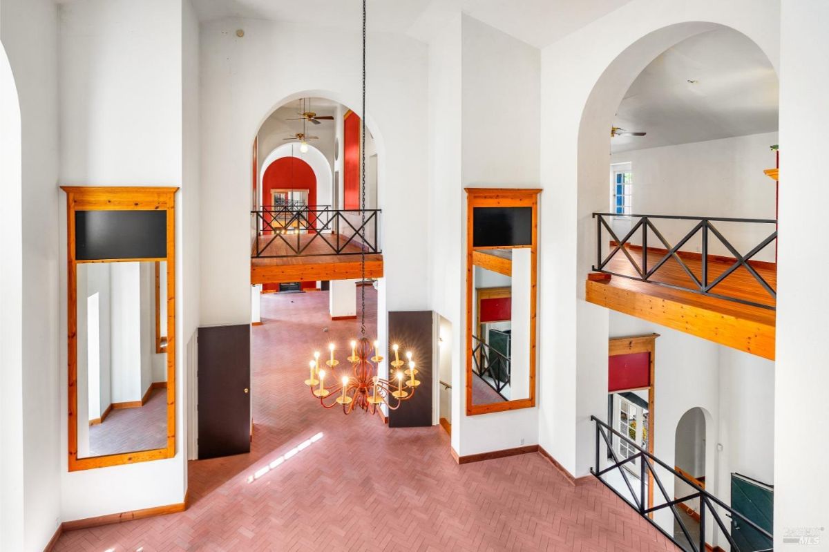 A view of a grand open interior with high ceilings, chandeliers, and wooden railings on upper levels.