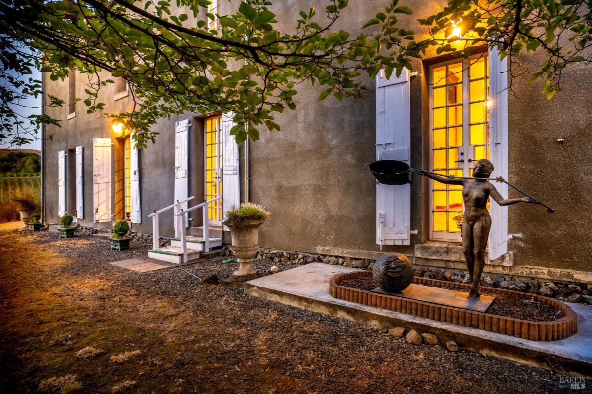 A side of the building with French doors, exterior lighting, and a decorative statue near a landscaped area.