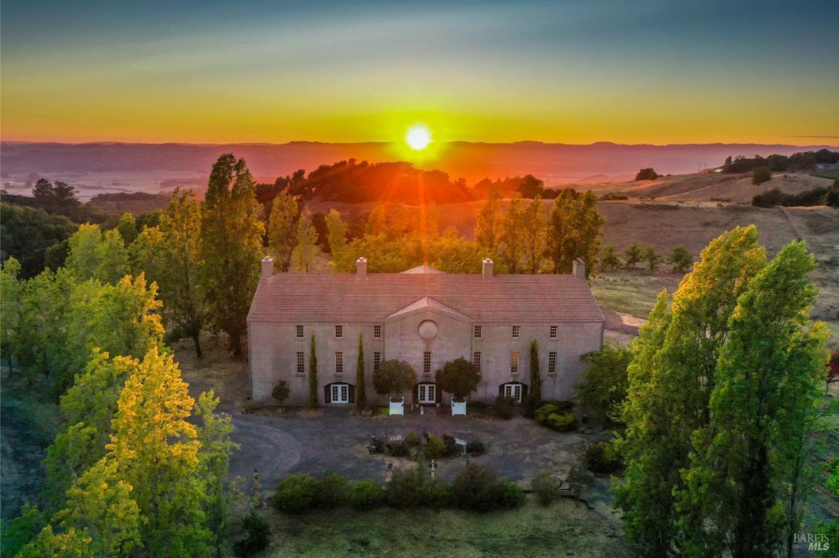 The same estate viewed closer, with the sun setting directly above the building, casting warm light.