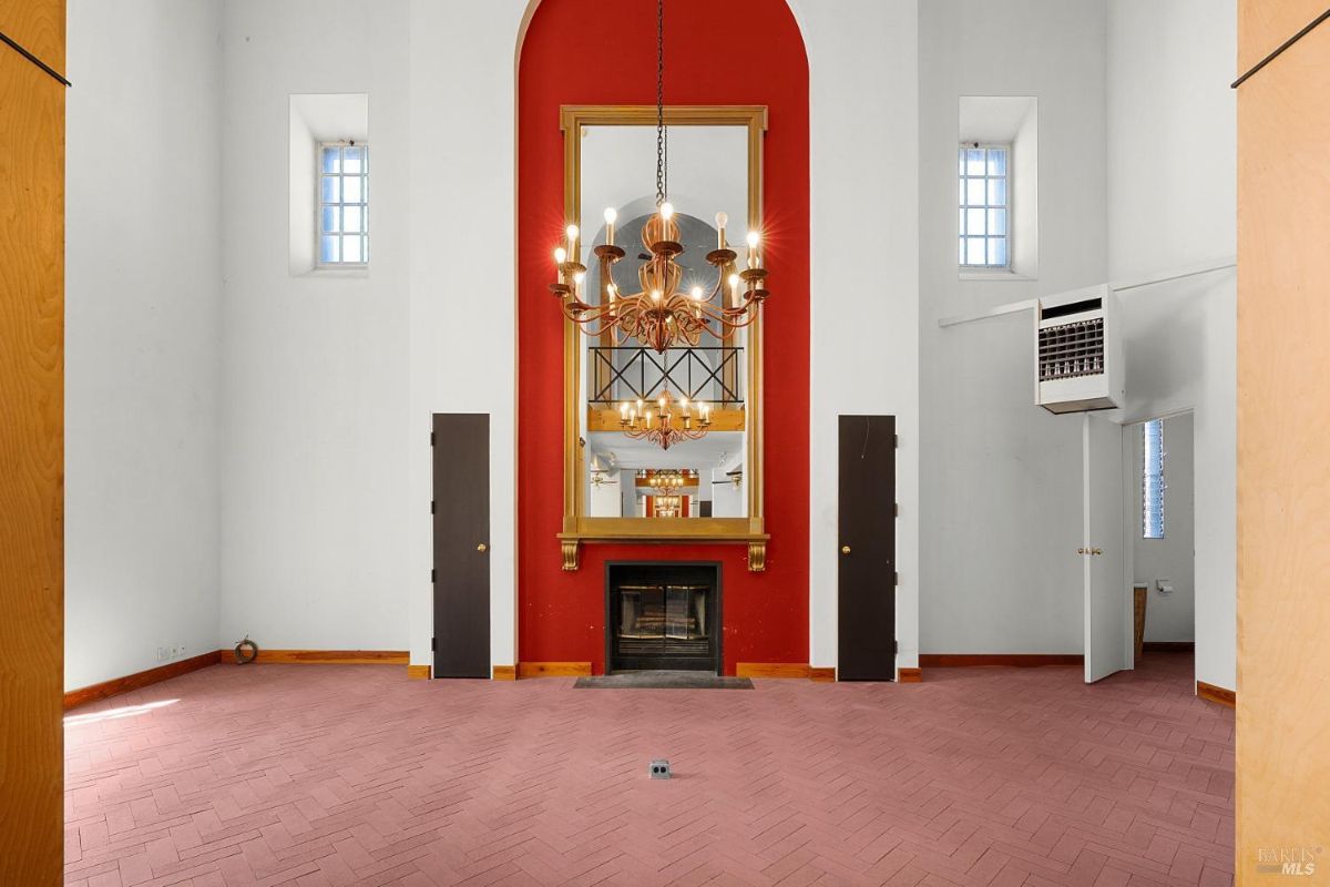 A room with a chandelier, red accent wall, and fireplace framed by tall mirrors, with high ceilings.