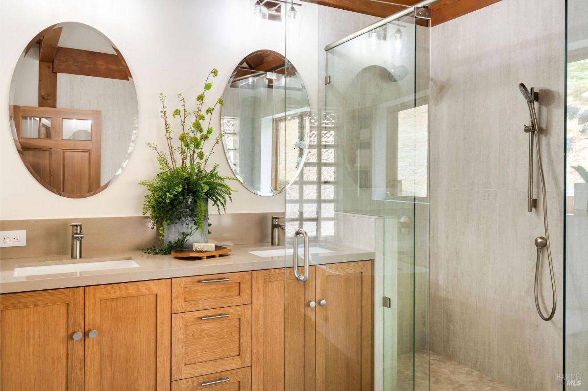 Modern bathroom with a double vanity, glass shower enclosure, and oval mirrors.